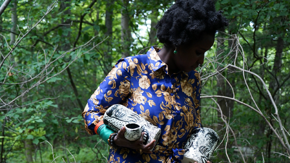 A woman standing in front of trees holds handmade ceramics.