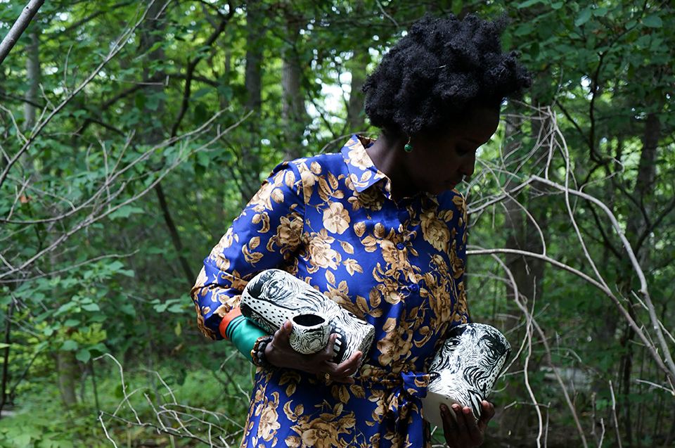A woman standing in front of trees holds handmade ceramics.