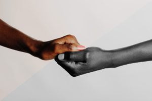 Two clasped hands, half of the image is in color and the other is black and white.